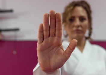 Das Bild zeigt eine Kampfsportlerin, die eine Hand in die Kamera mit der Handfläche in die Kamera hält, was als Geste der Abwehr gedeutet werden kann (verweist auf: „Safe Sport Code“: BISp fördert Projekt der Sporthoch­schule Köln)